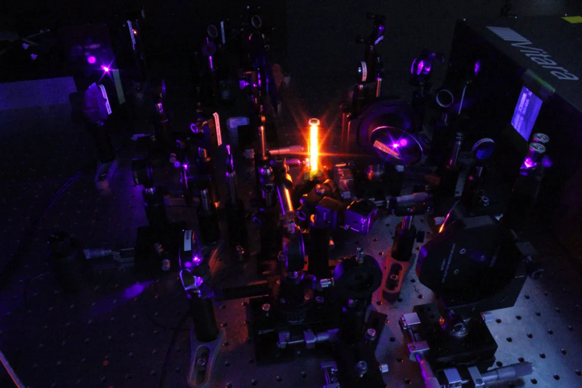 Optics on a table with bright orange fluorescence emitting from a central sample holder